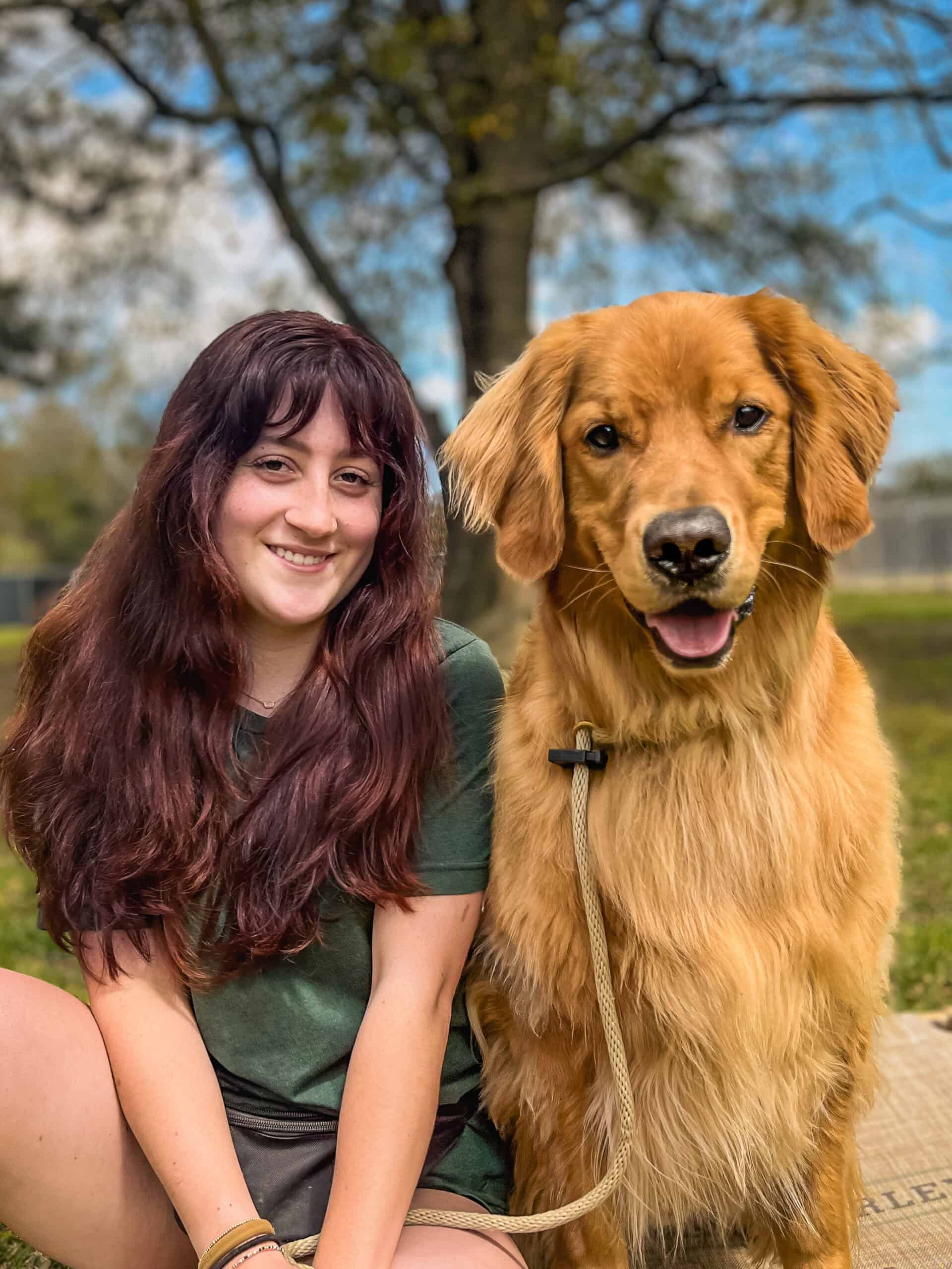 Caroline Ginn of Well Mannered Dog sitting outdoors next to a golden retriever on a long lead