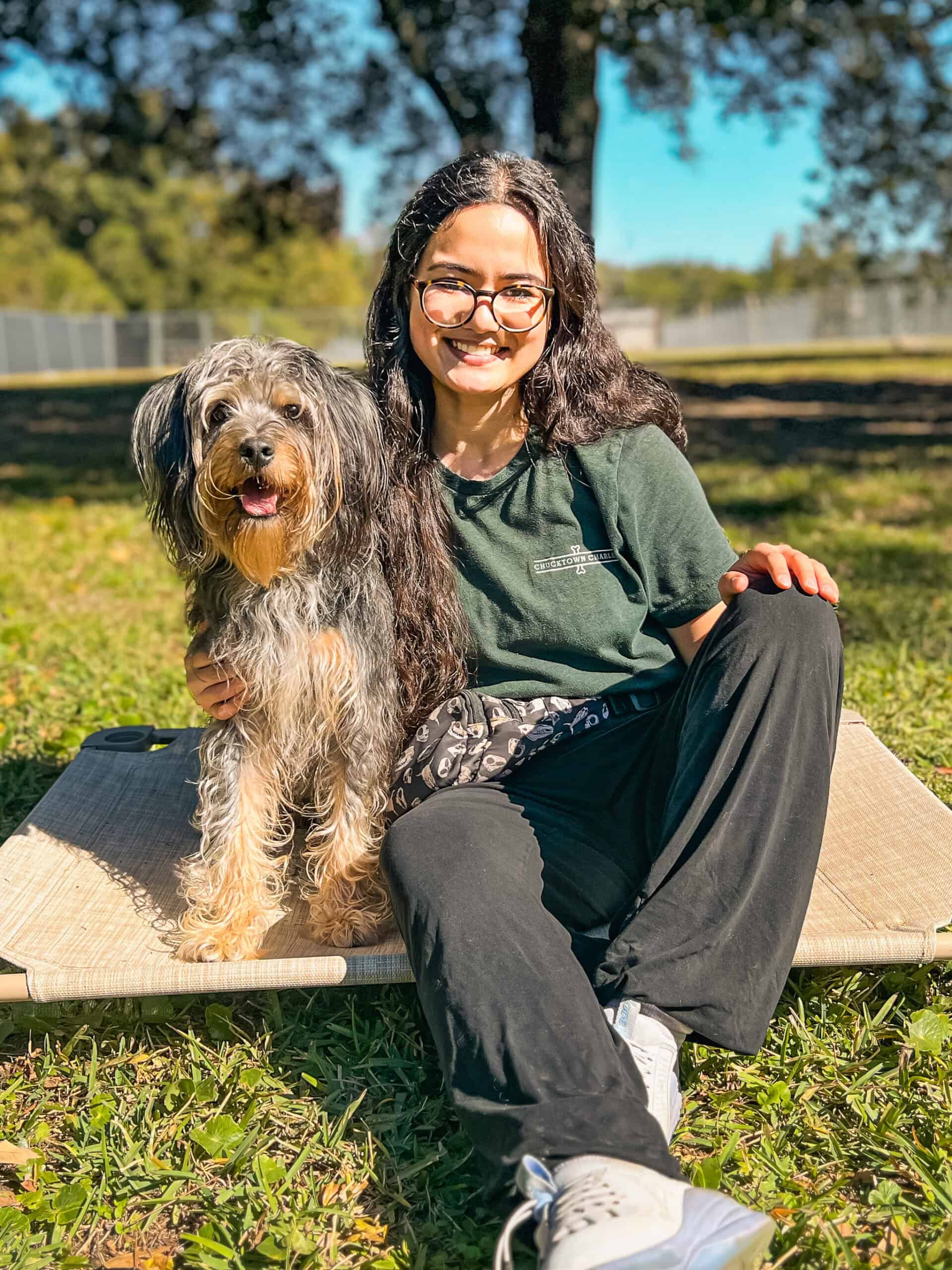 Kat Delp of Well Mannered Dog sitting outdoors beside her rescue dog Iroh on a raised cot